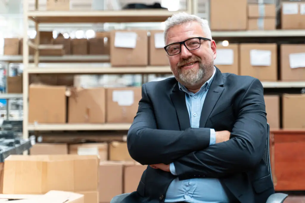 Business owner in his warehouse smiling at the camera with inventory on the shelves behind him